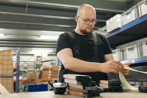 Ein Mann mit Brille sieht sich gelbe Etiketten an. Vor ihm liegen Produkte auf einem Tisch.