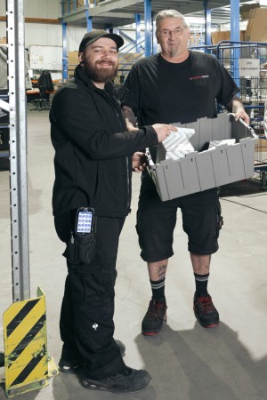 Zwei männliche Mitarbeiter halten eine graue Kiste aus Plastic.