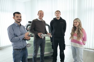 Drei Männer und eine Frau stehen vor einem türkisen Auto.