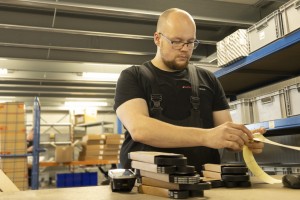 Lagerist in schwarzer Kleidung klebt Aufkleber auf Karton